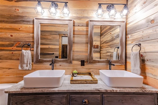 bathroom featuring double vanity, wooden walls, toilet, and a sink