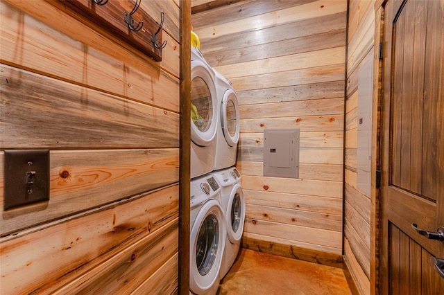 clothes washing area with wood walls, electric panel, laundry area, and stacked washer and dryer