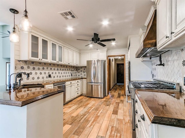 kitchen featuring visible vents, appliances with stainless steel finishes, a sink, wall chimney range hood, and a peninsula