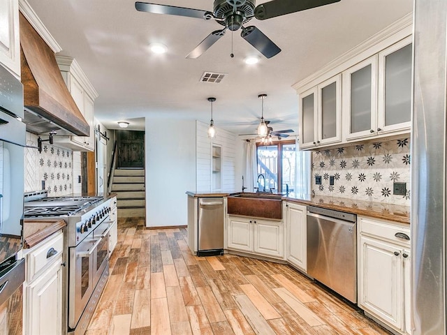 kitchen featuring visible vents, appliances with stainless steel finishes, a peninsula, light wood-style floors, and a sink