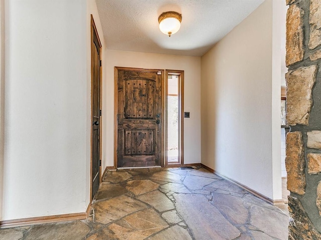 entrance foyer featuring a textured ceiling, stone tile flooring, and baseboards