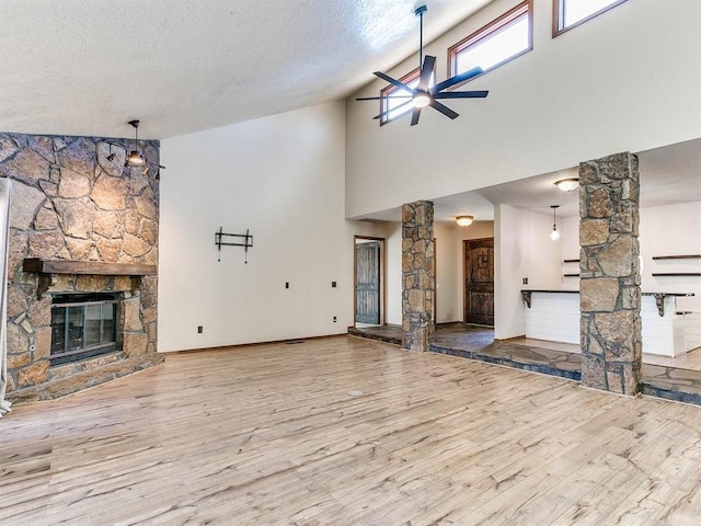 unfurnished living room featuring a fireplace, decorative columns, ceiling fan, a textured ceiling, and wood finished floors