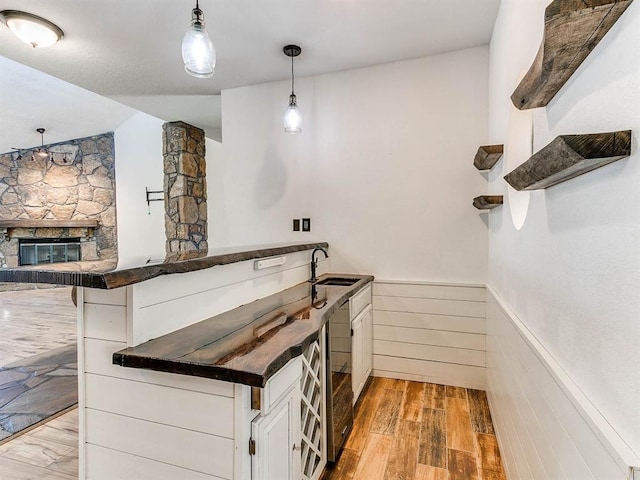 bar featuring a wainscoted wall, a fireplace, hanging light fixtures, a sink, and light wood-type flooring