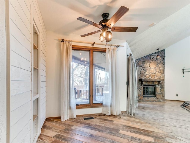 unfurnished living room featuring visible vents, ceiling fan, wood finished floors, vaulted ceiling, and a fireplace