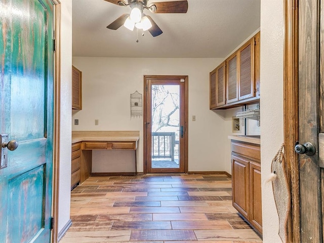 interior space with brown cabinets, light countertops, wood tiled floor, ceiling fan, and baseboards