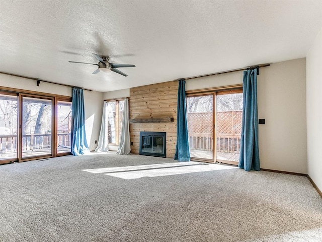 unfurnished living room featuring a large fireplace, baseboards, ceiling fan, a textured ceiling, and carpet flooring