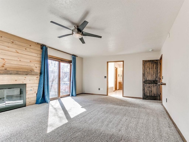 unfurnished living room with a textured ceiling, carpet, a glass covered fireplace, and baseboards