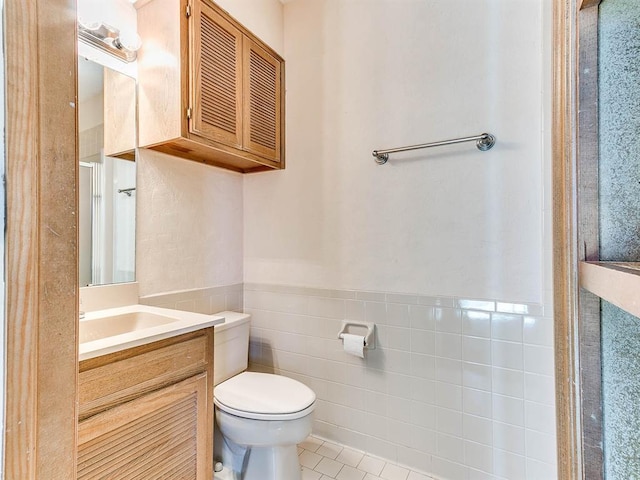 bathroom with toilet, a wainscoted wall, tile patterned floors, vanity, and tile walls