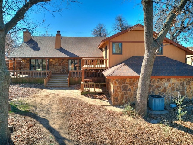 back of house with stone siding, central AC unit, a deck, and roof with shingles