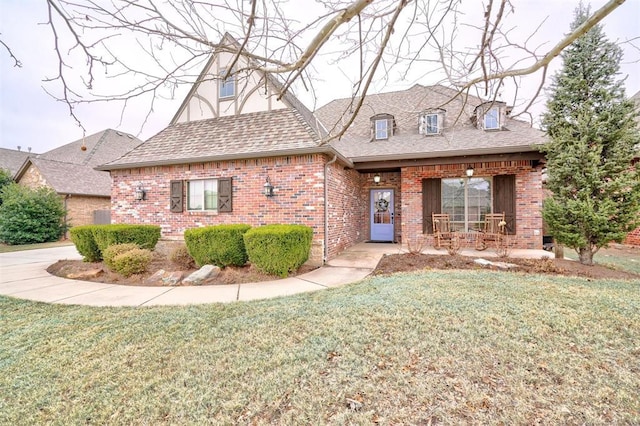 view of front of home featuring brick siding, a porch, a front lawn, and roof with shingles