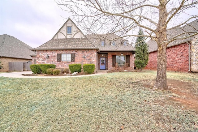 english style home with a shingled roof, a front lawn, and brick siding