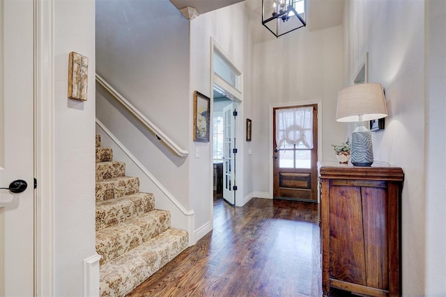 foyer entrance featuring baseboards, wood finished floors, a high ceiling, stairs, and a notable chandelier