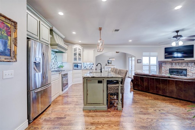 kitchen with arched walkways, a breakfast bar, open floor plan, appliances with stainless steel finishes, and light wood-type flooring