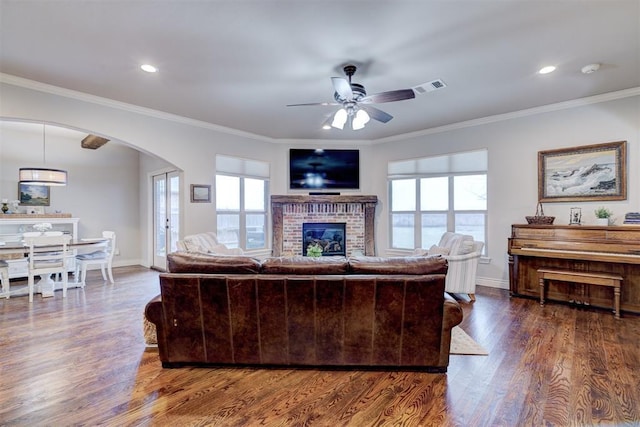 living area with arched walkways, a fireplace, visible vents, dark wood-type flooring, and ornamental molding