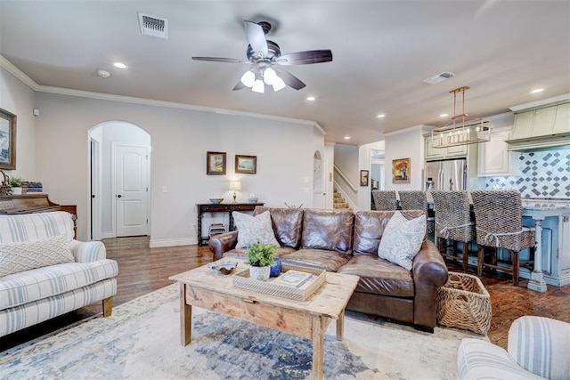 living area with arched walkways, visible vents, and crown molding