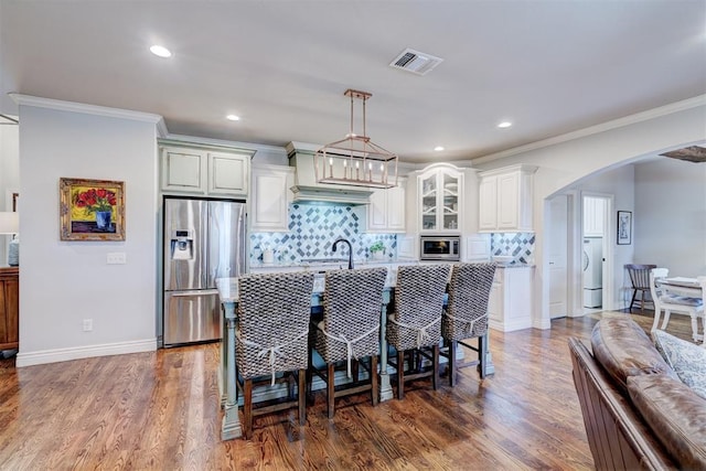 kitchen featuring a center island with sink, visible vents, arched walkways, appliances with stainless steel finishes, and dark wood-style flooring