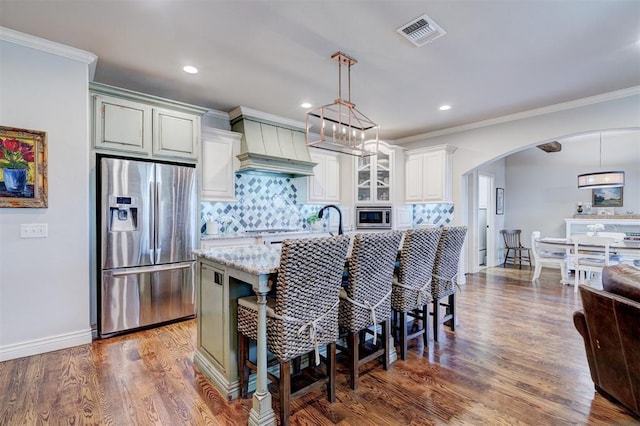 kitchen featuring arched walkways, appliances with stainless steel finishes, ornamental molding, light stone countertops, and custom exhaust hood