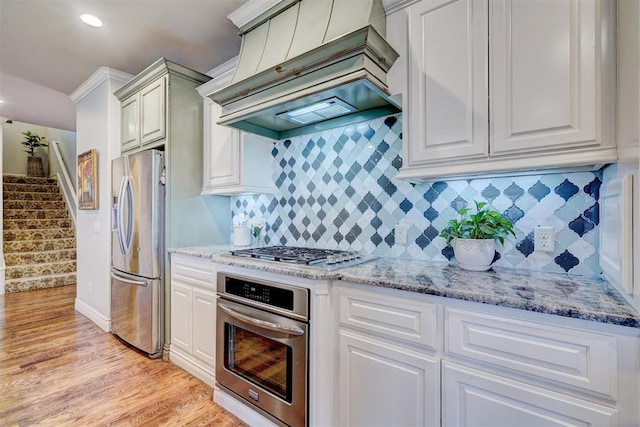 kitchen featuring custom exhaust hood, light wood-style floors, appliances with stainless steel finishes, and light stone countertops