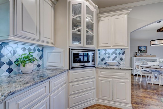 kitchen featuring dark wood-type flooring, white cabinets, light stone countertops, stainless steel microwave, and glass insert cabinets