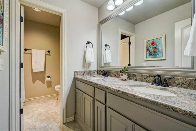 bathroom featuring double vanity, a sink, toilet, and baseboards