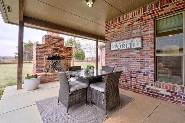 view of patio with an outdoor brick fireplace, outdoor dining space, and fence