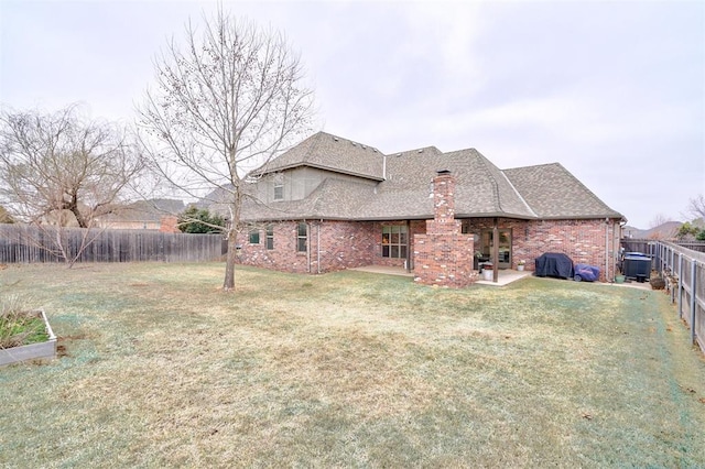 back of property with a fenced backyard, brick siding, a shingled roof, a lawn, and a chimney