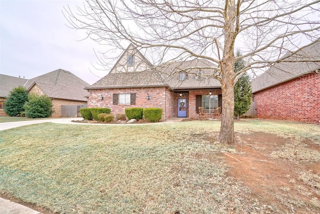 tudor-style house with a shingled roof, brick siding, and a front lawn