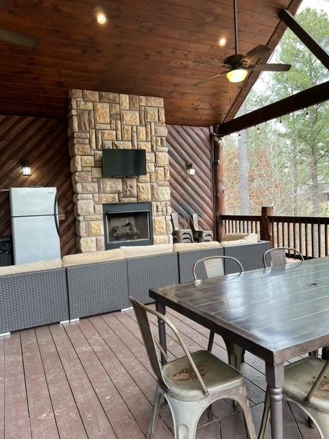 wooden deck featuring an outdoor stone fireplace, outdoor dining area, and a ceiling fan