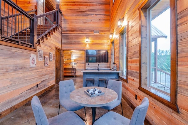 dining space with stairway, a towering ceiling, visible vents, and wooden walls