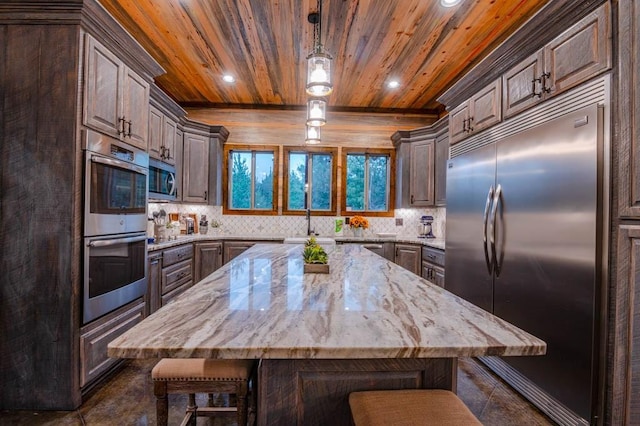 kitchen featuring wood ceiling, light stone counters, a breakfast bar, a center island, and stainless steel appliances