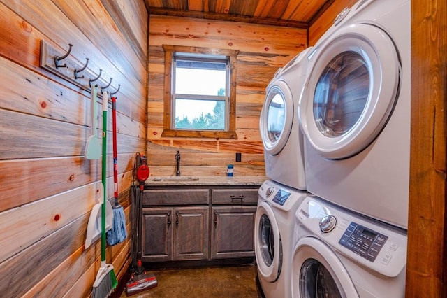 laundry room featuring cabinet space, wooden walls, wooden ceiling, stacked washing maching and dryer, and a sink