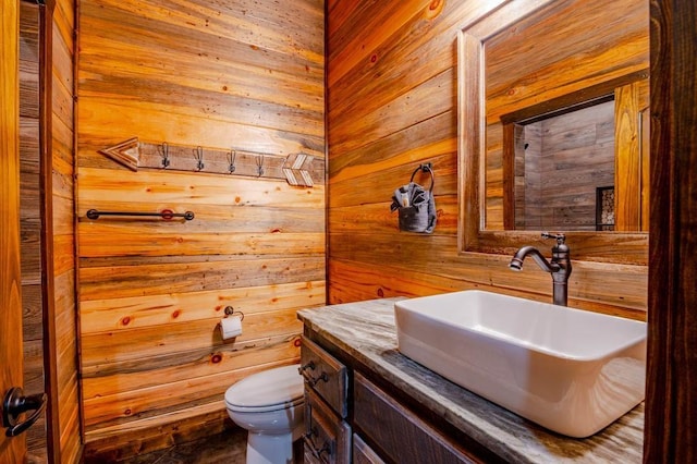 half bathroom with toilet, wood walls, and vanity