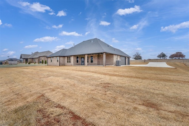 back of property with a yard, central AC, brick siding, and an attached garage