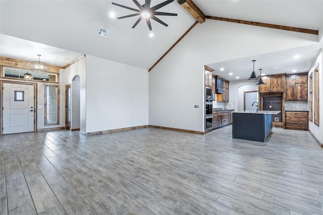 unfurnished living room with light wood-type flooring, arched walkways, visible vents, and beamed ceiling