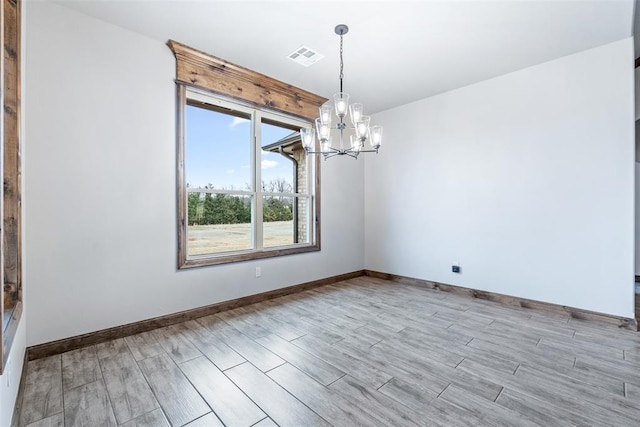 unfurnished room featuring baseboards, visible vents, an inviting chandelier, and wood finished floors