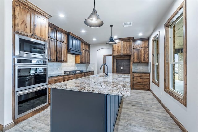 kitchen with visible vents, appliances with stainless steel finishes, light stone counters, decorative light fixtures, and a sink