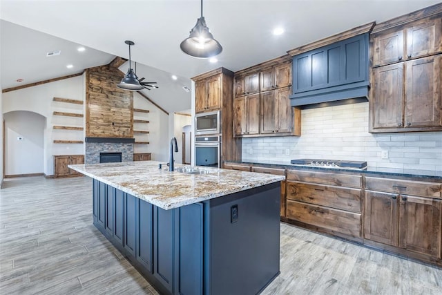 kitchen with stainless steel appliances, a fireplace, vaulted ceiling, light stone countertops, and light wood finished floors