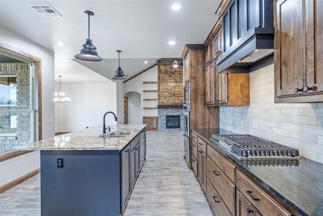 kitchen featuring light stone countertops, premium range hood, a sink, appliances with stainless steel finishes, and decorative backsplash