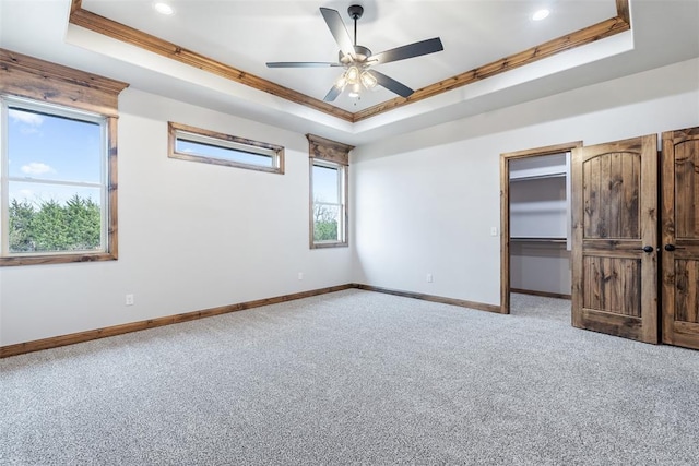 unfurnished bedroom featuring light carpet, a raised ceiling, a walk in closet, and baseboards