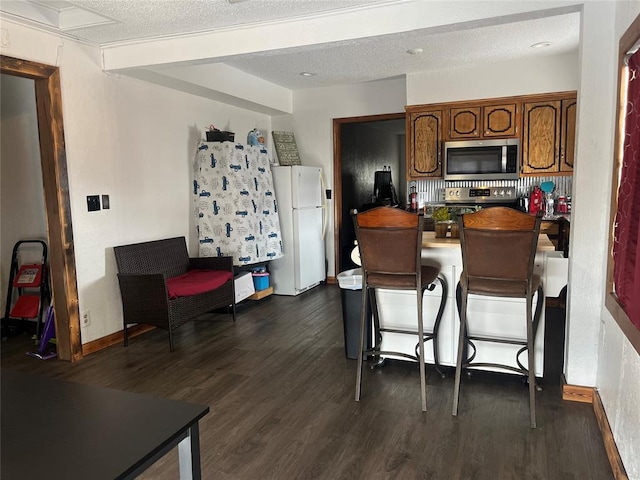 kitchen featuring a textured ceiling, dark wood-style flooring, a kitchen breakfast bar, appliances with stainless steel finishes, and brown cabinets