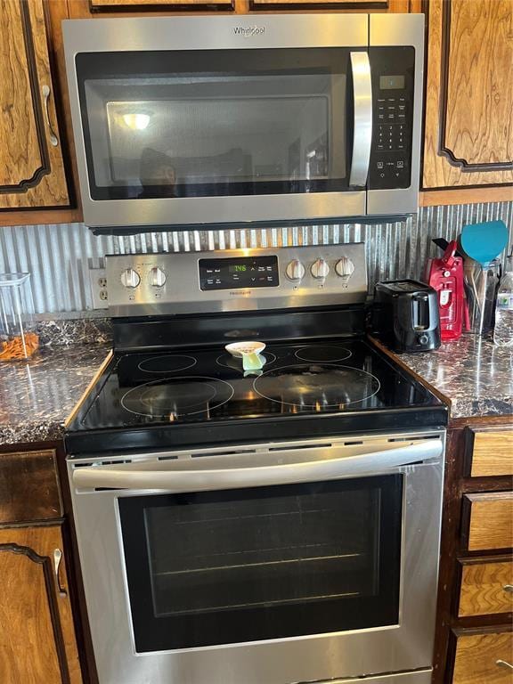 kitchen featuring stainless steel appliances, dark stone counters, brown cabinets, and backsplash