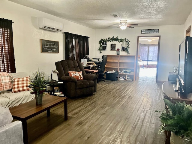 living area with a textured ceiling, ceiling fan, wood finished floors, visible vents, and a wall mounted AC