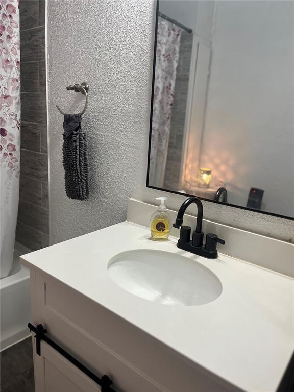 full bathroom with shower / bath combo, vanity, and a textured wall