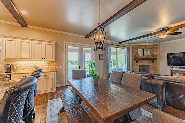 dining space with crown molding, a fireplace, dark wood-style floors, french doors, and a ceiling fan