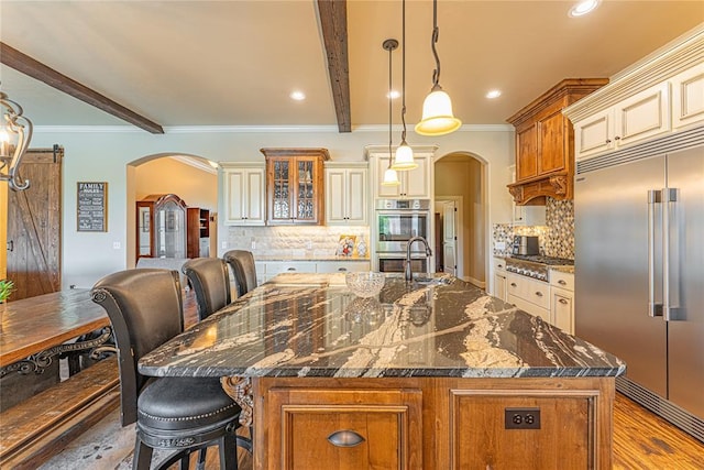 kitchen with cream cabinets, stainless steel appliances, arched walkways, and beam ceiling