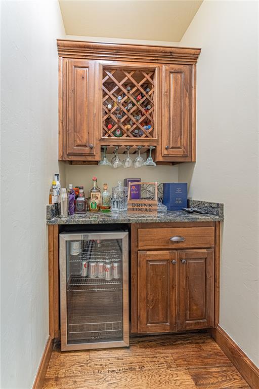 bar featuring wood finished floors, baseboards, a bar, and wine cooler