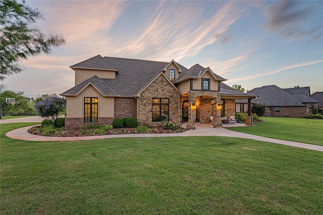 craftsman-style home featuring a front lawn, covered porch, stone siding, roof with shingles, and stucco siding