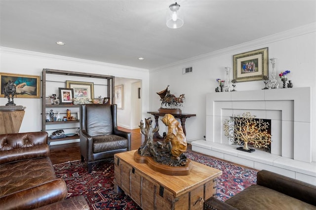 living area with a tile fireplace, wood finished floors, visible vents, and ornamental molding