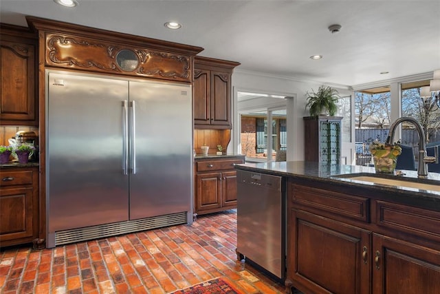 kitchen featuring a healthy amount of sunlight, stainless steel appliances, brick floor, and a sink