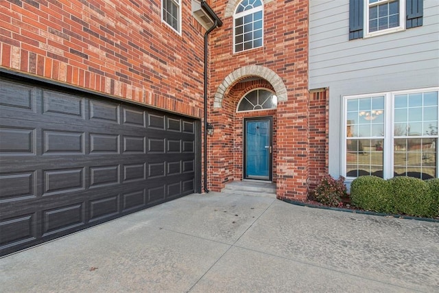 doorway to property featuring a garage, concrete driveway, and brick siding